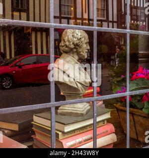 Eine Büste von William Shakespeare, die auf einigen Büchern steht, blickt aus einem Fenster auf die Gebäude im Tudor-Stil in Stratford-upon-Avon. Stockfoto