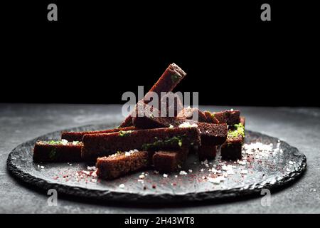 Schwarzes Brot Toast für Bier mit Knoblauchsalz und Kräutern auf schwarzem Hintergrund Stockfoto