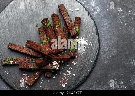 Schwarzbrotbiercroutons mit Knoblauchsalz und Kräutern auf schwarzem Hintergrund Stockfoto