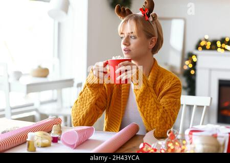 Schöne junge Frau trinkt heiße Schokolade und Verpackung Weihnachtsgeschenk zu Hause Stockfoto