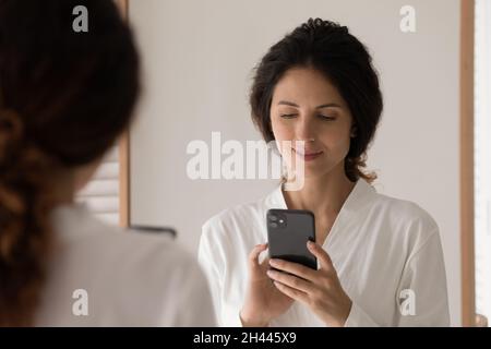 Hispanische Frau trägt Bademantelständer im Badezimmer mit Smartphone Stockfoto