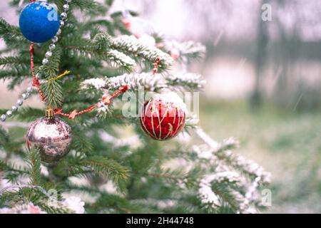 Draußen schneit es auf dem Weihnachtsbaum, der mit Spielzeug geschmückt ist. Wir feiern Neujahr und Weihnachten. Stockfoto