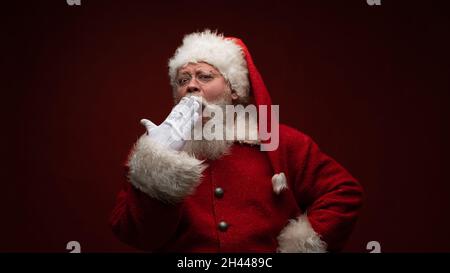 Der Weihnachtsmann gähnt, trägt eine Brille und einen Hut. Stockfoto