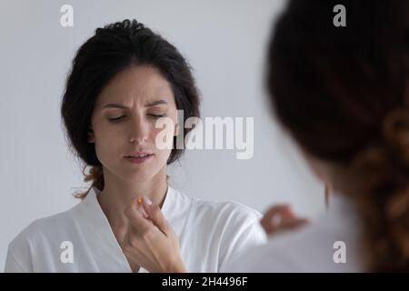 Junge, ungesunde Frau mit runzelndem Stirnrunzeln im Bademantel hält die Pille in der Hand Stockfoto