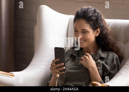 Hispanische Frau auf dem Sessel entspannt hält Handy lesen angenehme sms Stockfoto