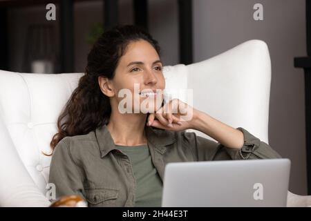 Attraktive junge Frau, die sich im gemütlichen Sessel mit Laptop entspannt Stockfoto