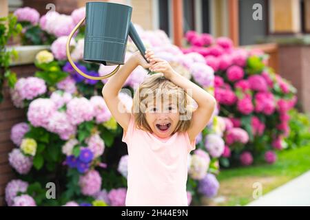 Lustige Kinder, die Blumen wässern. Kind im Garten bewässerte Blumen aus einer Gießkanne im Sommer. Kindergärtner hat Spaß genießt Pflege Stockfoto