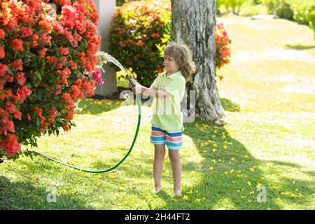 Glücklicher Junge gießt Wasser aus einem Schlauch. Amerikanische Kinder Kindheit. Kinder bewässern Blumen im Garten. Gartenarbeit im Haus. Stockfoto