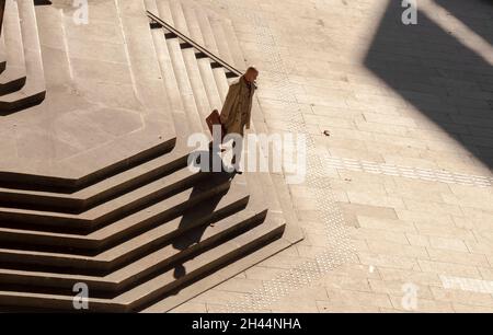 Belgrad, Serbien - 25. Oktober 2020: Ein kahlköpfiger Mann in Anzug und Mantel mit Aktentasche, der alleine die riesige öffentliche Treppe hinuntergeht, mit Blick aus dem hohen Winkel Stockfoto