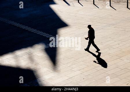 Belgrad, Serbien - 25. Oktober 2020: Ein reifer Mann mit Mütze, der alleine über den gepflasterten Platz der Stadt läuft, mit Blick aus einem hohen Winkel und Schatten Stockfoto