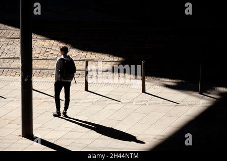 Belgrad, Serbien - 26. Oktober 2020: Ein Jugendlicher, der allein auf eine Straßenbahn wartet, die im Sonnenlicht auf der Bushaltestelle steht, mit Blick von hinten, mit Shad Stockfoto