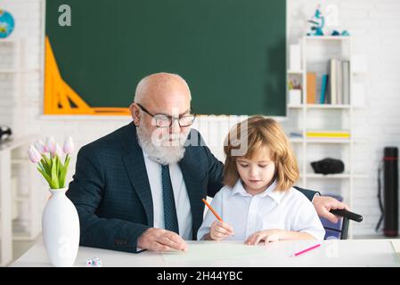 Schüler lesen und schreiben mit Lehrer im Klassenzimmer. Alter Lehrer und kleiner Schuljunge. Privatunterricht. Stockfoto