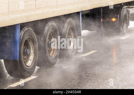 LKW mit trockenem Lieferwagen, der tagsüber auf einer nassen Straße mit Spritzern unterwegs ist Stockfoto