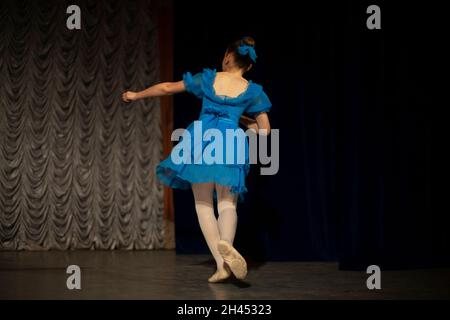 Ein Kind tanzt auf der Bühne. Performance eines Mädchens in einem blauen Kleid. Der Künstler zeigt Rock and Roll. Ein Kind in einer Tanzstunde. Stockfoto