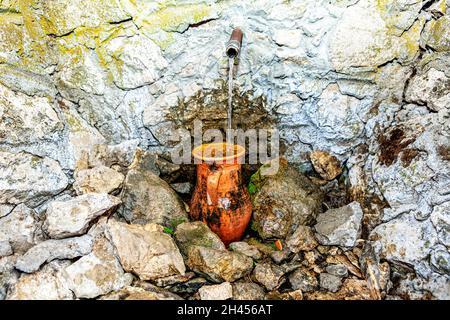 Quellwasser fließt in den Krug. Natürliche Quelle von Trinkwasser . Krug in den Steinen Stockfoto
