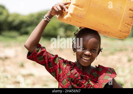 Porträt eines lächelnden schwarzen Africn-Mädchens, das einen Wasserkanister auf dem Kopf trägt Stockfoto