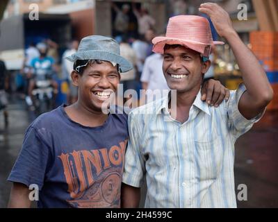 Zwei fröhliche, lächelnde und lachende Portiers auf einem Fischmarkt in der Nähe des Crawford Market in Mumbai, Indien, mit billigen Plastikmützen zum Tragen nasser Lasten Stockfoto