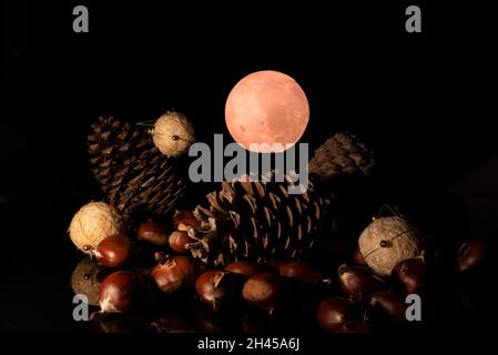 weihnachtsstillleben mit Tannenzapfen, weihnachtskugeln, Kastanien und dem roten Mond im Hintergrund. Schwarzer Hintergrund. weihnachtskonzept. Stockfoto