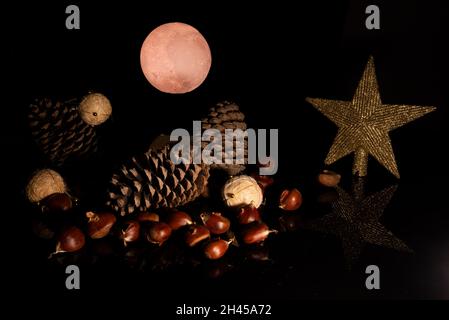weihnachtsstillleben mit Tannenzapfen, weihnachtskugeln, Sternkastanien und dem roten Mond im Hintergrund. Schwarzer Hintergrund. weihnachtskonzept. Stockfoto