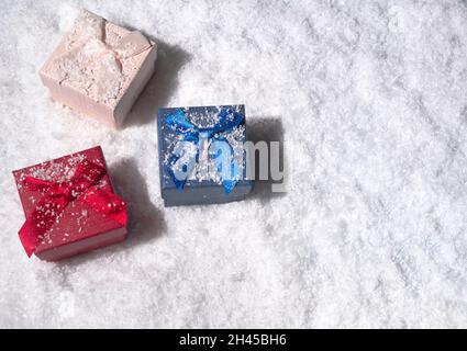 Rote, rosa und blaue Geschenkschachteln, die mit Schnee bedeckt sind. Flach liegend, Draufsicht. Minimaler Winterurlaub Konzept. Mit Kopierbereich. Stockfoto