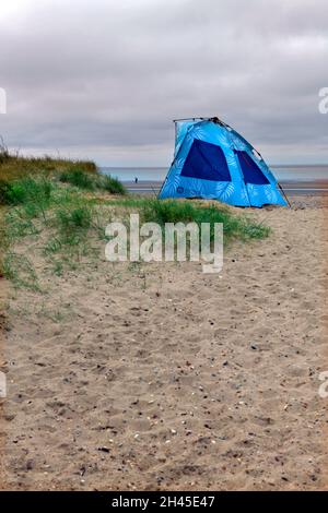 Einsame kleine Figur und Pop-up-Strand Schutz auf Beac bei holme neben dem Meer im Norden norfolk england Stockfoto