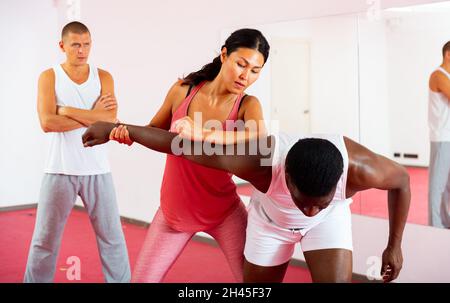 Selbstverteidigungstrainer lehrt asiatische Frau Stärke Techniken in Sporthalle Stockfoto
