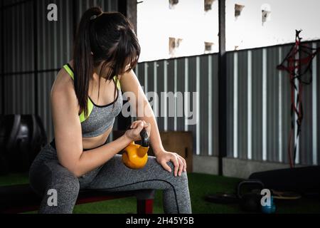 Junge asiatische Frau genießen das Training mit dem Heben Wasserkocher Glocke mit einer Hand in der Turnhalle. Sport Bodybuilding Konzept. Stockfoto