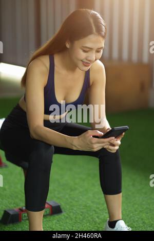 Gesund fit Mädchen sitzt im Health Club mit modernen Handy. Schöne Frau in Sportkleidung mit Smartphone. Stockfoto