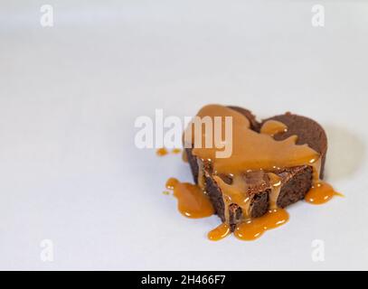 Herzförmiger Schokoladenkuchen, der mit einer gooey Caramel Sauce tropft Stockfoto