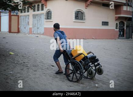 Gaza, Palästina. Oktober 2021. Ein palästinensisches Kind schleppt in einem armen Viertel am Stadtrand von Khan Yunis im südlichen Gazastreifen einen Rollstuhl mit einer Kanister Wasser. Kredit: SOPA Images Limited/Alamy Live Nachrichten Stockfoto