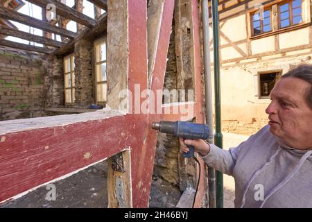Dernau, Deutschland. Oktober 2021. Der Altbau-Renovierer Linah entfernt mit einem Heißluftgebläse die alte Farbe von den Balken eines Fachwerkhauses, von dem die Flut nur ein Skelett zurückließ. Die tödliche Sturzflut im Ahrtal hat auch Hunderte historischer Fachwerkhäuser beschädigt oder zerstört - Bewohner und Behörden versuchen, so viele wie möglich zu retten. (Zu dpa: Fachwerkhäuser auch von Hochwasser betroffen - viele zu retten). Quelle: Thomas Frey/dpa/Alamy Live News Stockfoto
