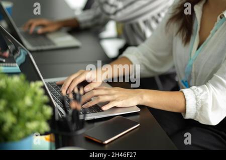 Beschnittenes Bild von Geschäftsmitarbeitern, die an ihrem Arbeitsplatz am Laptop arbeiten und schreiben. Stockfoto