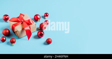 Schöne Weihnachten rote Kugeln und Neujahrsgeschenk mit einem roten Band Dekoration Spielzeug auf blauem Hintergrund. Weihnachtskonzept für das neue Jahr. Flach festlich Stockfoto