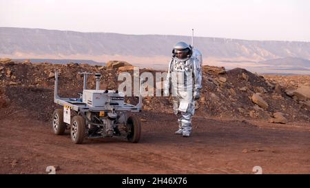 Ein analoger Astronaut, gekleidet in einen speziellen Raumanzügen, umläuft einen Rover auf dem Gelände der Mars-ähnlichen Forschungseinrichtung, die für die AMADEE-20-Mars-Simulation am Ramon-Krater in der Negev-Wüste in Israel gebaut wurde. Sechs Analogastronauten aus Israel, Portugal, Spanien, Deutschland, den Niederlanden und Österreich haben eine dreiwöchige Isolation innerhalb der Forschungseinrichtung abgeschlossen und konnten ihren Lebensraum nur in Raumanzügen verlassen. Das Team führte eine Reihe von wissenschaftlichen und technologischen Experimenten durch, in der Hoffnung, die Grundlagen für zukünftige bemannte Missionen zum Mars zu schaffen. Stockfoto