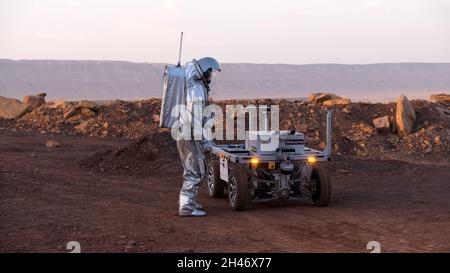 Ein analoger Astronaut, gekleidet in einen speziellen Raumanzügen, umläuft einen Rover auf dem Gelände der Mars-ähnlichen Forschungseinrichtung, die für die AMADEE-20-Mars-Simulation am Ramon-Krater in der Negev-Wüste in Israel gebaut wurde. Sechs Analogastronauten aus Israel, Portugal, Spanien, Deutschland, den Niederlanden und Österreich haben eine dreiwöchige Isolation innerhalb der Forschungseinrichtung abgeschlossen und konnten ihren Lebensraum nur in Raumanzügen verlassen. Das Team führte eine Reihe von wissenschaftlichen und technologischen Experimenten durch, in der Hoffnung, die Grundlagen für zukünftige bemannte Missionen zum Mars zu schaffen. Stockfoto