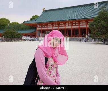 Nahaufnahme eines Porträts einer jungen asiatischen muslimischen Frau mit Hijab und Brille im Hof des heian-Schreines. Fröhlicher, aufgeregt und fröhlicher Ausdruck. Stockfoto