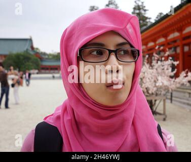 Nahaufnahme eines Porträts einer jungen asiatischen muslimischen Frau mit Hijab und Brille im Hof des Schreines in Japan. Aufgeregt, glücklich und Ente Gesichtsausdruck. Stockfoto
