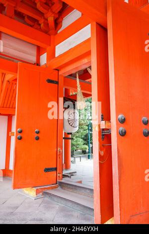 Blick auf die große orangefarbene Holztür mit dekorativer japanischer weißer Laterne am Haupttor des Heian-Schreins. Keine Personen. Stockfoto