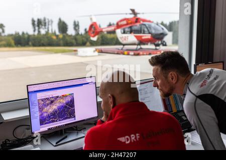 PRODUKTION - 11. Oktober 2021, Baden-Württemberg, Villingen-Schwenningen: Die Piloten Matthias Fleisch (l) und Roy Fleischer schauen sich das Flugwetter der kommenden Nacht auf einem Monitor an, während ihr Hubschrauber im Hintergrund steht. Der Rettungshubschrauber Christoph 54 ist der einzige in Baden-Württemberg, der auch Nachtflugkapazitäten hat. Die Nachtcrew mit den beiden Piloten übernimmt die fliegende Intensivstation von 6.30 Uhr abends bis 7 Uhr am nächsten Morgen. Sie ist auf der Station Villingen-Schwenningen des Deutschen Luftrettungsdienstes (DRF) stationiert und fliegt Einsätze von t Stockfoto