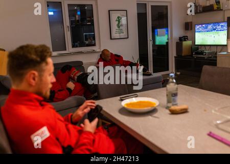 PRODUKTION - 11. Oktober 2021, Baden-Württemberg, Villingen-Schwenningen: Die Piloten des Rettungshubschraubers Roy Fleischer (l-r) und Matthias Fleisch blicken auf ihre Smartphones, sitzen vor ihrem Abendessen und liegen auf dem Sofa. Der Rettungshubschrauber Christoph 54 ist der einzige in Baden-Württemberg, der auch Nachtflugkapazitäten hat. Die Nachtmannschaft mit den beiden Piloten übernimmt die fliegende Intensivstation von 18:30 Uhr abends bis 7:00 Uhr am nächsten Morgen. Sie ist auf der Station Villingen-Schwenningen des Deutschen Luftrettungsdienstes (DRF) stationiert und fliegt Einsätze fr Stockfoto