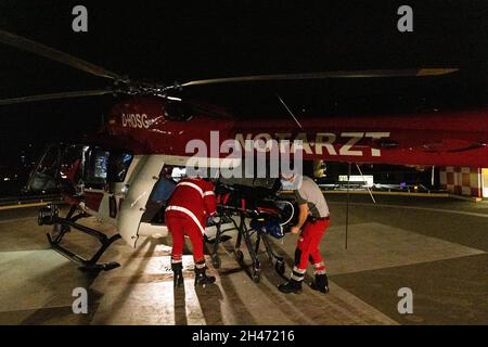 PRODUKTION - 11. Oktober 2021, Baden-Württemberg, Stuttgart: Benjamin Lehmann (r), Notarzt und HEMS-TC (Helicopter Emergency Medical Services Technical Crew Member), entlädt zusammen mit Notarzt Dr. Christoph Herzog (l) den Patienten aus dem Rettungshubschrauber, der auf dem Hubschrauberlandeplatz am Katharinenhospital abgestellt ist. Der Rettungshubschrauber Christoph 54 ist der einzige in Baden-Württemberg, der auch Nachtflugkapazitäten hat. Die Nachtcrew mit den beiden Piloten übernimmt die fliegende Intensivstation von 6.30 Uhr abends bis 7 Uhr am nächsten Morgen. Es ist stationiert in Stockfoto