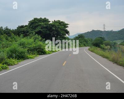 Bewässerungs- und Transportsystem, offene Kurve Asphaltstraße entlang des Kanals mit Berg- und Hochspannungsturm in Thailand Stockfoto