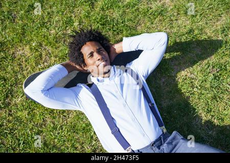 Schwarzer Geschäftsmann, der sich mit seinem Skateboard auf dem Rasen ausruht Stockfoto