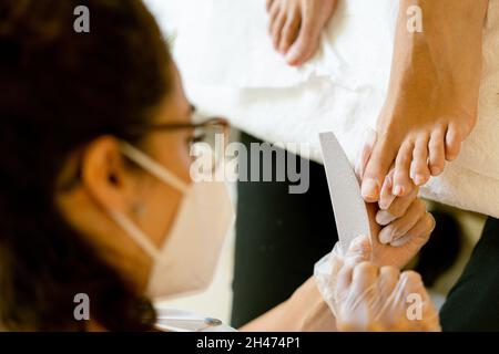 Kosmetikerin, die eine Pediküre malt, um die Nägel ihrer Kundin in einem Beauty-Center zu malen. Stockfoto