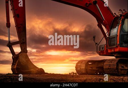 Baggerlader auf der Baustelle geparkt, nachdem Boden gegraben wurde. Bulldozer auf Sonnenuntergang Himmel und Wolken Hintergrund. Bagger nach der Arbeit. Maschine mit Erdbewegung Stockfoto