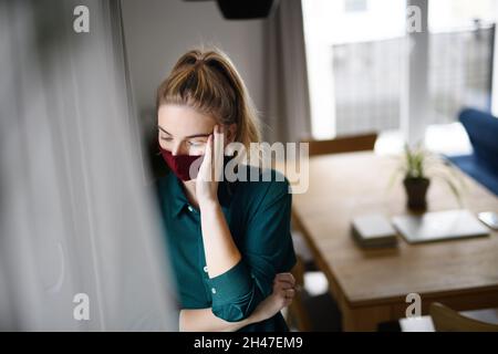 Porträt einer traurigen jungen Frau mit Gesichtsmaske drinnen zu Hause. Stockfoto