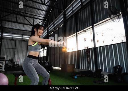 Junge asiatische Frau genießen das Training mit dem Heben Wasserkocher Glocke mit einer Hand in der Turnhalle. Sport Bodybuilding Konzept. Stockfoto