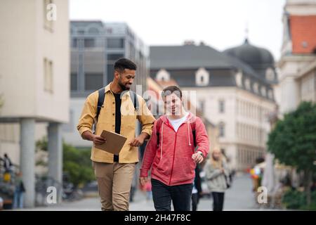 Junger Mann mit Down-Syndrom und sein Mentor-Freund gehen und reden im Freien Stockfoto