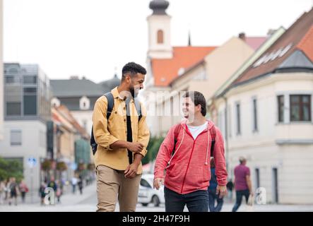 Junger Mann mit Down-Syndrom und sein Mentor-Freund gehen und lachen im Freien Stockfoto