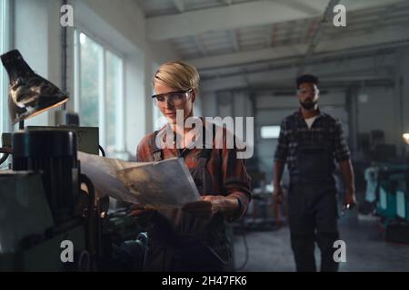 Porträt junger birazialer Industriekollegen, die in Innenräumen in einer Metallwerkstatt arbeiten, lächelnd. Stockfoto